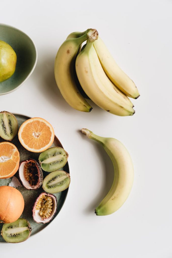 Assorted tropical fruits including bananas, kiwis, and oranges on a white surface, perfect for healthy eating concepts.