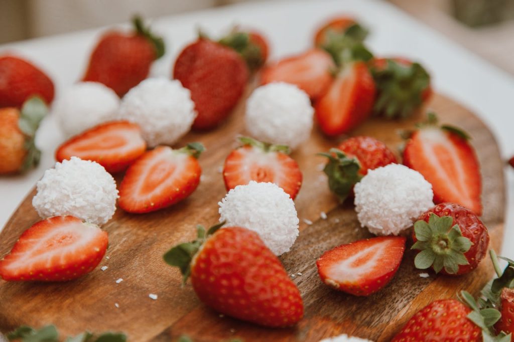 Appetizing strawberries and coconut balls arranged on a wooden board, perfect for dessert lovers.